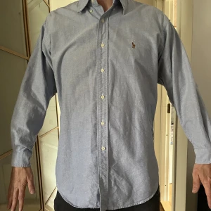 Skjorta Ralph Lauren  - Blå skjorta från Ralph Lauren, storlek 16/33, vilket motsvarar typ storlek M. 16 tum är halsvidden och 33 tum är armlängden. Personen på bilden är 183 cm lång och väger ca 80 kg.