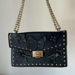 Väska med nitar - Jättefin väska i skinnimitation med guld- och fjärilsdetaljer. L: 26cm H: 15cm B: 8cm