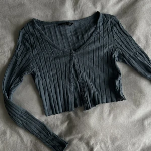 Blå kofta  - Topp/kofta som har ”lettuce hem” och knappdetaljer. Croppad och tight åtsittande. 