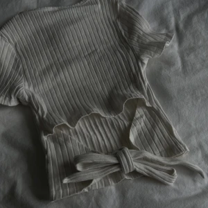 Vit top med knytning på ryggen  - Knytdetalj och öppen rygg på baksidan. ”Stickat” tyg. Tight. 