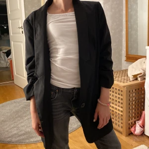 Jättesnygg svart kavaj - Kavaj med fin skurning och knapp fram. 🔥❤️ Trekvartsärm. Två framfickor. Storlek 38. 🌟 Rem bak för att justera passform. Knappt använd. 👍🏻Säljer för 200 kr + frakt. 😊 Min dotter på bilden och därför ser kavajen lång ut - den är egentligen höftlång.