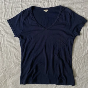 T-shirt med pärlor  - Mörkblå T-shirt med snygg pärldetalj, köpt secondhand och har en liten fläck strax under nyckelbenet men inget som stör!! Annars i bra skick🌷