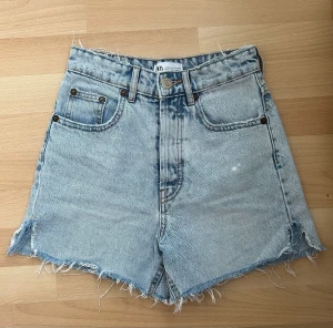 Zara shorts denim i hög midja  - Shorts. Hög midja. Detalj med slitsar på sidorna och ofållad kant. Fem fickor. Knäppning med metallknappar. Knappt använda. 
