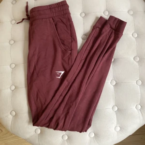 Gymshark  - Gymshark mjukis från kollektionen Pippa. Storlek XS, färgen Burgundy. Säljs ej längre. Använda en gång men där är ett håll i ena byxfickan, va så när jag fick dem, inget som syns och går att sy igen.