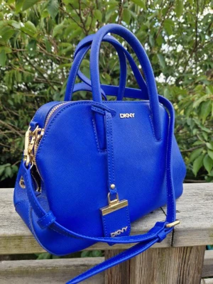 DKNY väska  - Snygg blå dkny väska som är i  fint skick (förutom en liten defekt på handtaget som man ser på ena bilden) Har både handtag och avtagbar axelrem. Bredd 26cm, höjd 17cm, djup 11cm. Nypris 2000kr säljer för 800kr plus frakt.