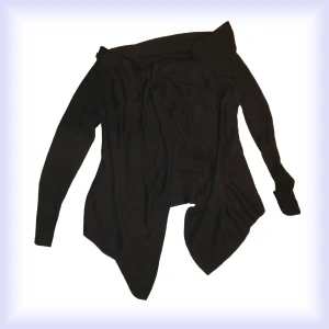 Stickad Enkel Cardigan / Kofta - Enkel cardigan med ribbade ärmar ner till slutet. Längre vid sidorna och extra tyg i nacken för en lös/oversized look. Har ett hål mot kanten av dem längre sidorna, något som man kan däremot gömma och lär inte märkas.