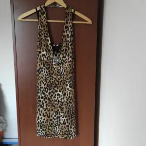 Snygg topp/kort klänning i leopardmönster och avtagbart paljettsmycke. Vintagefeeling. I nyskick och oanvänd. Färg: svart, brun, guld, beige.