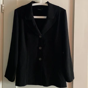 Svart kavaj  - Svart kavaj, med två kapar på sidan, två extra knappar, 93% polyester 7% Spandex 