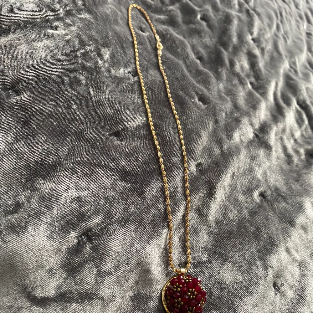 Ett fint guld halsband med en vinröd blomma. Accessoarer.