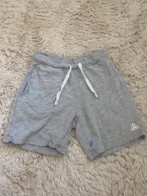 Grå mjukis shorts - Ett par grå lite längre mjukis shorts i storlek 122/128, de har en liten blå fläck som man ser på bild två men annars väl andvända