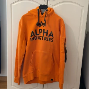 Alpha Industries Hoodie  - En orange Alpha Industries hoodie med en svart patch 