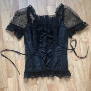 Korsett - En svart korsett med vackra detaljer och spets på, köpt här på Plick, säljer då den inte kom till användning. Korsetten är i bra skick, finns däremot ett hål i spetsen på baksidan på ena ärmen och lite lösa trådar.