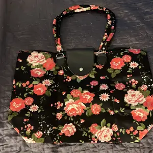 En väska men rosa blommer på och en svart bas. Den är helt ny och oanvänd men har ingen prislapp på. Den är i ett perfekt skick på grund av att den inte använts. 
