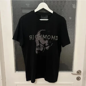 John Richmond tshirt - En skitsnygg och askön tisha från John Richmond. Köpt på Zgander. Nyskick på den då jag endast använde den en gång. Fick den i present för ca 1,5 år sedan och säljer den då den är för stor och bara legat i garderoben. Nypris: 2000. Mitt pris: 700