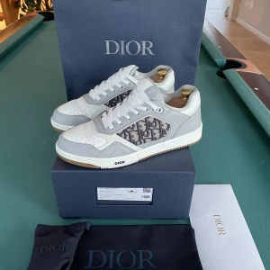 Dior B27 Low-top Sneaker - Dior B27 Low-top Sneaker Färg: Grey and white Nypris: 11308kr Mitt pris: 6500kr Skick: 8,5 (Använda cirka 5 gånger)  Följande ingår: Påse Dustbag Låda Kvitto Oanvända extra skosnören   OBS: Skoblock ingår ej!