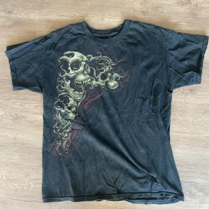 tshirt med dödskallar  - tshirt med dödskallar köpt på beyond retro ungefär 2019!!kommer tyvärr aldrig till användning av mig står ingen storlek i den men skulle uppskatta till ungefär en large! 