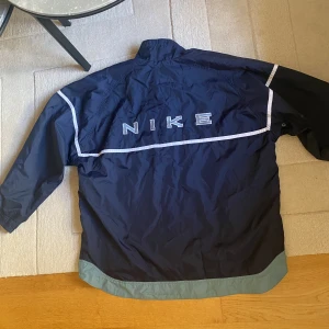 Vintage Nike windbreaker  - Vintage Nike windbreaker i storlek XL. Aldrig använd av mig då den var alldeles för stor. Märkte att den hade några pyttesmå fläckar på baksidan som jag kan skicka bild på. Annars i superbra skick. dragsko där nere så man kan dra in den.
