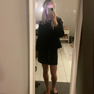 Mockakjol med knappar - Svart kjol i mockaimitation med silvriga knappar. Minikjol i A-linjeform