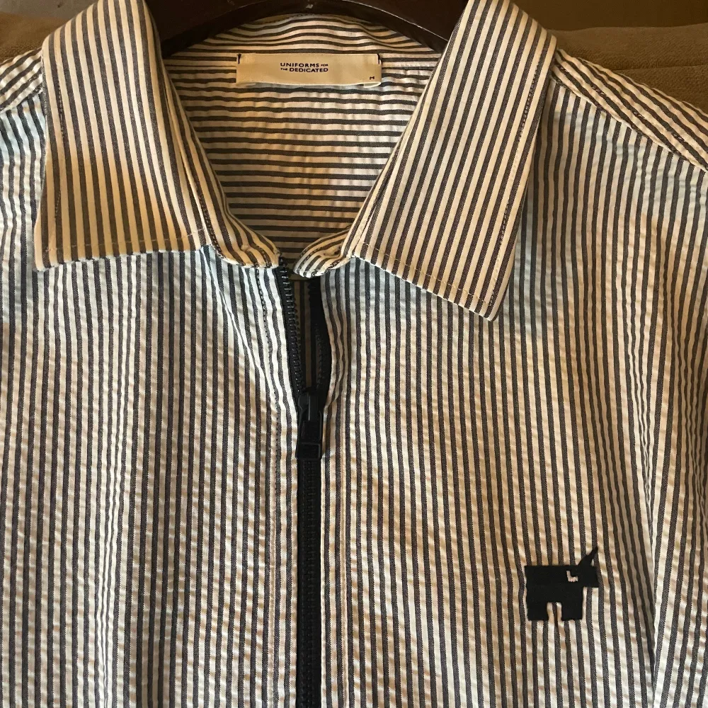 Kortärmad kritstrecksrandig skjorta i crinkled bomull. Med svart dragkedja och märkets logga embroderad på bröstet. Väldigt unik och otrolig bra kvalitet skjorta köpt på NK för ca 1200kr. Skjortor.