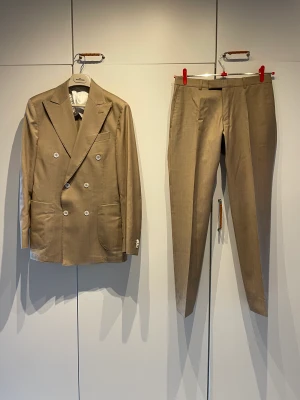 Oscar Jacobson kostym - Beige dubbelknäppt kostym från Oscar Jacobson i linne. Perfekt till sommaren, studenten och balen. Den är storlek 46 och slim fit. Använd färre än 5 gånger alltså som helt ny! Säljer för att den inte passar mig. Skriv för frågor eller bilder! Inga returer