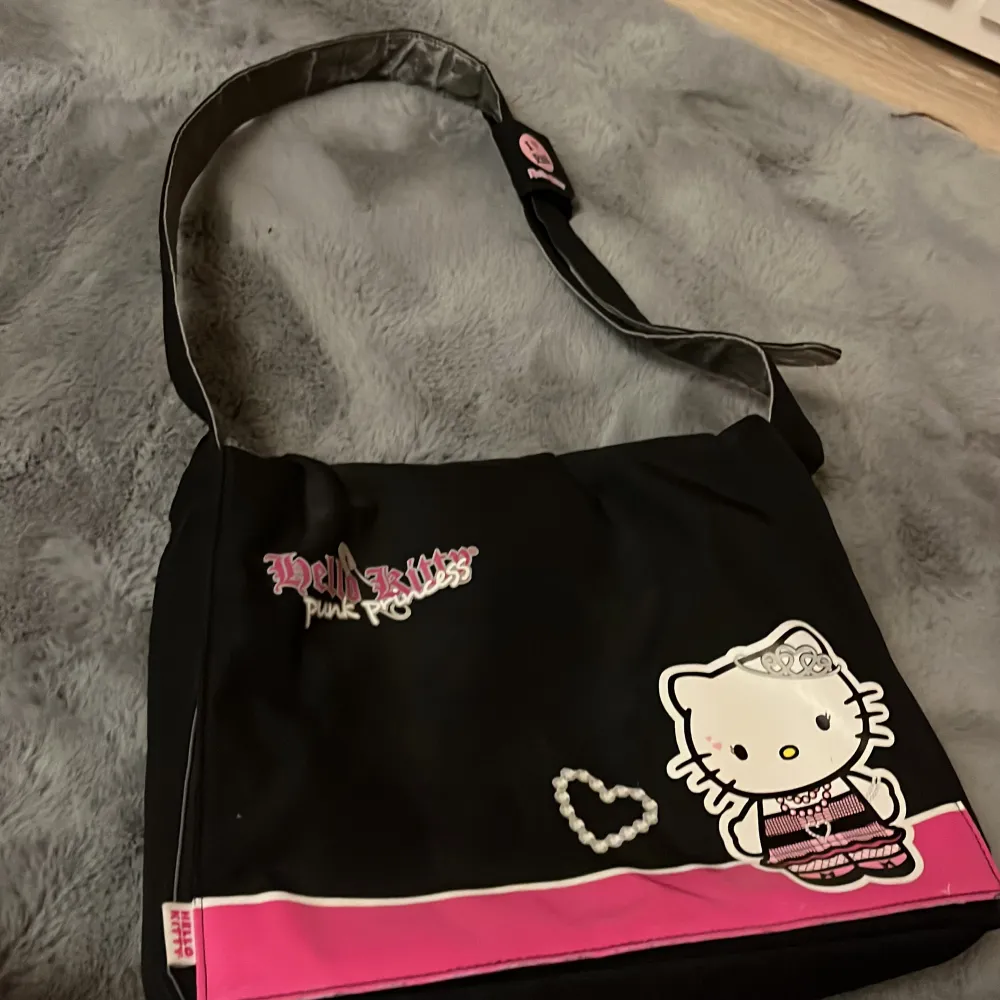 En hello Kitty väska med axelrem. Den är svart utanpå och rosa inuti. Väskan har jättegulliga hellokitty detaljer😺💕Skriv om ni vill ha flera bilder! . Väskor.