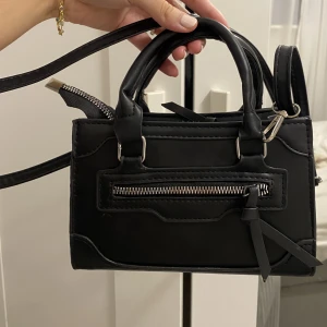 Svart axelremsväska - Säljer denna fina söta svarta väska. Aldrig använd. Går att ta bort banden samt justera de. Super fin och rymmer bra. Använder ej då jag har liknande.