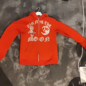 Aim for the moon zip hoodie - En aim for the moon tröja i storlek  M och färgen röd.  Ett få tal stenar har lossnat men inget man tänker på. Tveka inte på att skriva om du har någon fråga