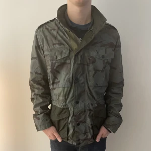 Tommy hilfiger Camo Field Jacka Strl M - Säljer en camo field jacka från Tommy hilfiger i strl M. Jackan är i nyskick och har inga tecken på användning. Modellen är 180 cm och väger 67kg. Nypris på jackan är 2999kr mitt pris är 699 kr. Skicka meddelande vid funderingar eller fler bilder. 