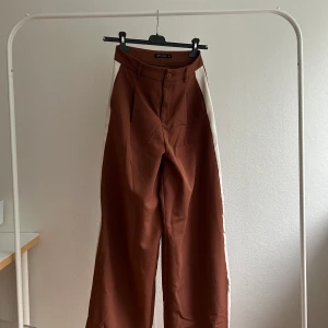 Vida tailored byxor  - Bruna byxor med ett vitt streck längs benen. Vida och straight legged.