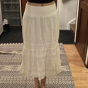 Vit lång kjol med spets detaljer - Intressekoll! Jätte fin oanvänd vit kjol perfekt för vår, sommar och tidig höst. Jätte fina mönster, köptes i Wien, Österrike, enda exemplaret kvar! Inbyggd underkjol och jätte bekvämt material runt midjan 🤍