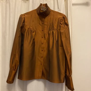 Fantastisk vintage blus - Fantastiskt snygg vintage blus i rostbrun färg. Krås i halsen och vackra knappar även i ärmslut. Passar både en person i storlek 38 och 36. Vintage, troligen 60-tal.
