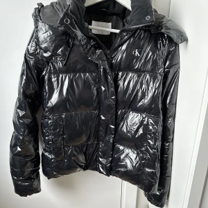 Svart Dunjacka - Dunjacka från Calvin Klein. Jackan är liten i storleken så även om det står m är den mer lik en s. Det finns inga defekter och är supervarm o skön. Luvan är löstagbar. 