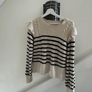 Randig Stickad tröja  - Randig stickad tröja med fin brodering. På bilden ser de ut som att tröjan är mer är de beiga håller, men den är mer vit i verkligheten och ränderna är mörk mörk blå! Super skön i materialet och den har  söta volanger på axlarna! Aldrig använd heller! 😊 