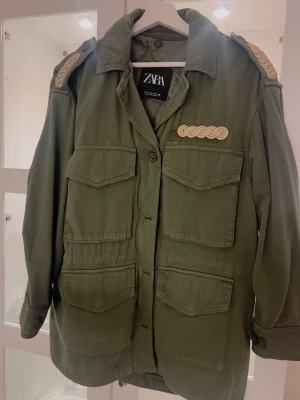 Jättefin grön jacka army med foder från Zara stl s - Jättefin army jacka från zara med knappar dragkedja fram med guld detaljer på axlar . Använd en gång avtagbart vadderat foder inuti fästs med knappar. Nypris 899:-