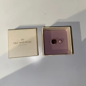 Lily & Rose ring & örhängen - Helt nya och oanvända Lily & Rose örhängen och ring. Guld och lila färgat. Råkade slänga returförpackning och kvitto så kunde inte lämna tillbaka. Orginalpris 900kr