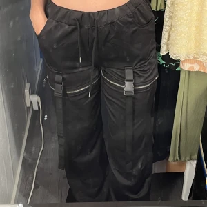 Byxor - Svarta byxor med dragkedja som man helt kan ta av nedre delen av byxorna. Har en lös passform vid benen men både resår och knytsnlten vid midjan.