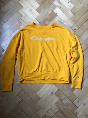 Champion sweatshirt - Gul tröja från Champion, ganska tunn i tyget. Köpt på plick, säljer vidare då jag inte använder den. Liten fläck på bröstet, se bild. I övrigt fint skick. 