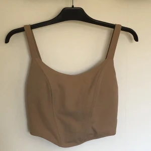 Beige fest topp i stl L - En beige snygg topp perfekt för fest. Toppen är från boohoo och har fortfarande lappen på. Toppen är i nytt skick och är i storlek L.Den har en dragkedja på baksidan och bh inlägg. På höger sida av toppen har några stygn släppt, dock inte särkilt synligt.