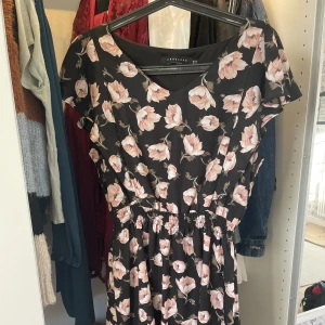 Festklänning - Superfin klänning i fint material. Den har korta ärmar som hänger löst över axeln, och är smått V-ringad framtill. Ganska kort, passar på t.ex dop eller middag. Det står M i men jag skulle säga S/M.