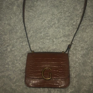 Väska från guess - En brun axelbands väska från guess köpt för ungefär 1200 kr