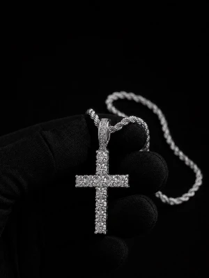 Cordell Halsband Med Diamant Kors - Säljer ett silverfärgat halsband med ett korsformat hänge som är täckt av gnistrande pärlor. Kedjan har ett tvinnat mönster och hänget är riktigt blingigt, perfekt för dig som gillar att sticka ut. Passar dig som vill ha något snyggt och trendigt runt halsen.