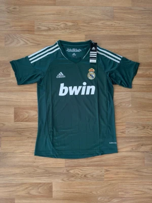Äkta Real Madrid Ronaldo #7 2012/13 Adidas S - Äkta Real Madrid adidas-tröja från 2012/13 med Ronaldo #7 på ryggen.  Storlek: S Modell: Tredjetröja Färg: Grön Sponsor: bwin Teknik: Climacool Tags kvar Mycket fint skick  Bild på produktkoden finns för att styrka äktheten. Fler bilder och mått skickas gärna vid intresse.