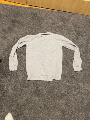 Ljusgrå sweatshirt från Polo Ralph Lauren - En stilren ljusgrå sweatshirt från Polo Ralph Lauren. Tröjan har rund halsringning, ribbade muddar vid ärmslut och nederkant samt en klassisk passform. Perfekt för en clean och avslappnad look.