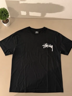 Svart Stüssy t-shirt med logga - Säljer en svart t-shirt från Stüssy med deras ikoniska vita logga tryckt på bröstet. Klassisk passform och rund halsringning, perfekt för en streetwear-look. Tillverkad i mjuk bomull för skön känsla hela dagen.