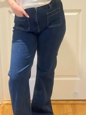 Mörkblå utsvängda jeans med fickor - Ett par 5-ficks medelhöga jeans i återvunnen bomullsblandning. Jeansen har utsvängda ben, fickor fram och bak och stängs med dragkedja och knapp framtill. Jeansen har stretch och figurnära passform. True to size men vart lite stora för mig därför aldrig använda💓