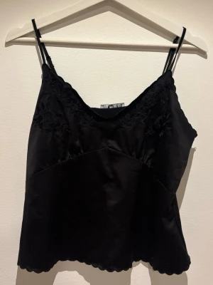 Linne / Festtopp - Snyggt svart linne i satin med broderade spetsdetaljer upptill och vågig kant 