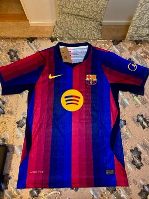 FC Barcelona 26/27 Lamine Yamal - Säljer en officiell FC Barcelona matchtröja från Nike med Lamine Yamal och nummer 10 på ryggen. Tröjan har klassiska blå och röda vertikala ränder, gul Nike-logga och Spotify som sponsor på bröstet. Tillverkad i lätt funktionsmaterial, perfekt för fotbollsträning.player version 