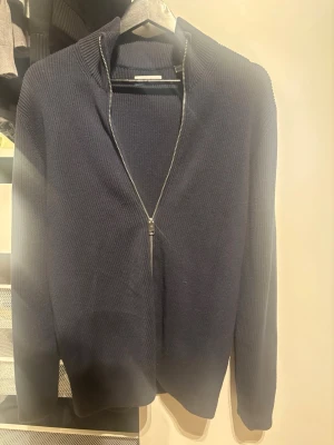 Jack&Jones zip tröja  - Snygg mörkblå ribbstickad tröja med dragkedja framtill och hög krage. Tröjan har långa ärmar och är tillverkad i ett mjukt, tjockare material som passar perfekt när det är kyligt ute. Enkel och stilren design som funkar till det mesta.