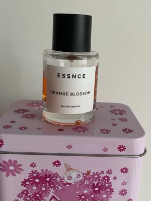 ESSNCE Orange Blossom parfym - Fräsch Eau de Parfum från ESSNCE med doft av orange blossom. Flaskan är cylindrisk i genomskinligt glas med svart rund kork och enkel vit etikett med svart text. Innehållet har en varm orange ton som ger en lyxig känsla. Mängd enl bild. Har förvarats mörkt och svalt 