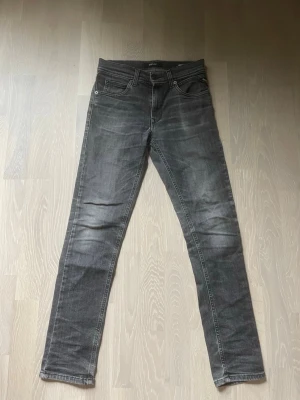 Grå slim fit jeans - Säljer ett par grå slim fit jeans med klassisk femficksdesign och snygga slitningar. Jeansen har normal midja och raka ben, tillverkade i stretchigt denimtyg för skön passform. Perfekta för en avslappnad och trendig look.